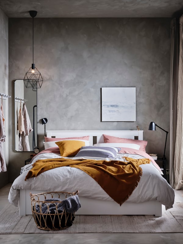 Chambre à coucher d'inspiration industrielle avec cadre de lit simple, miroir en métal noir, suspension et lampadaire noires et linge de lit gris, jaune et rose