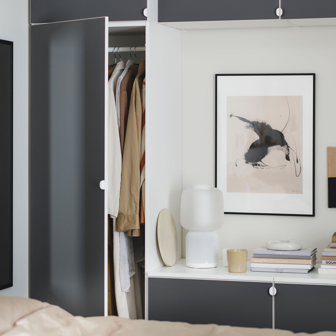 Une combinaison de penderie PLATSA en blanc avec une porte ouverte remplie de vêtements. Un miroir et une lampe sont placés à côté.