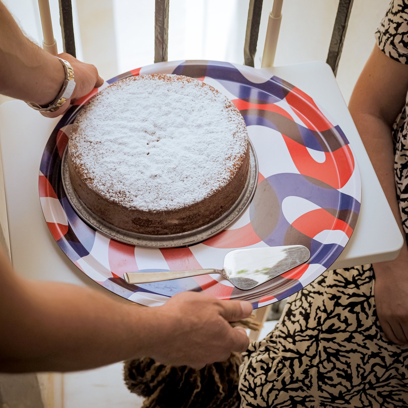 A woman carries a baked cake on a FRAMKALLA tray.
