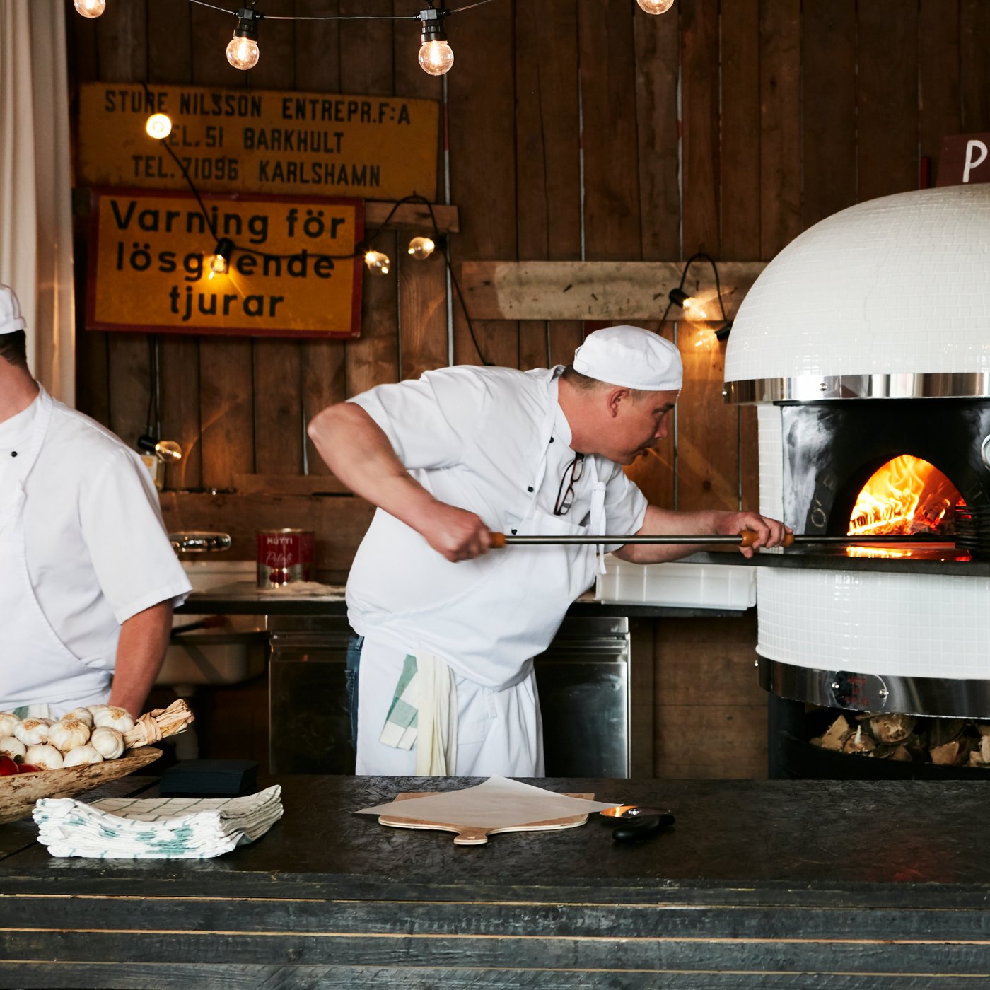 Un homme tenant une pelle à pizza en bois place une pizza dans un four dans un restaurant.