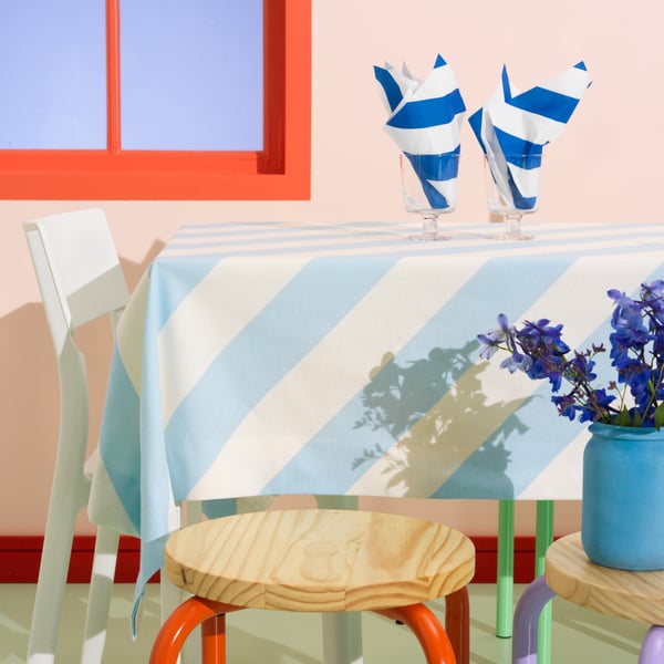 A table covered with a cloth made of LAGERMISPEL pre-cut fabric is set with two goblets filled with folded HAVSKATT napkins.