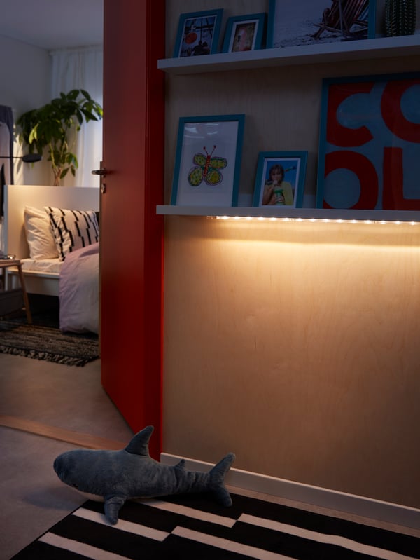 Space outside a bedroom where an LED lighting strip softly lights up the floor from underneath a picture ledge.