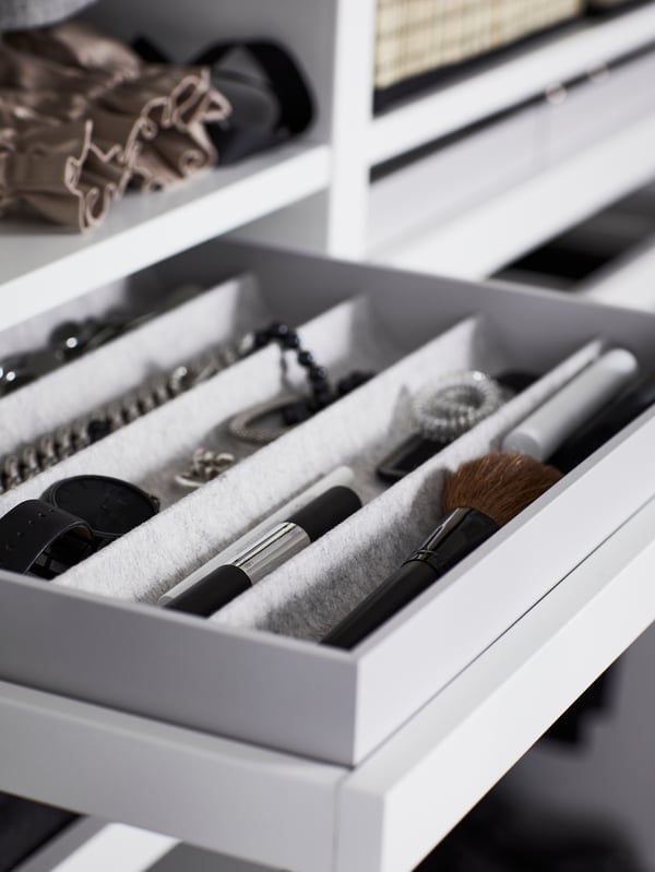 White pull-out tray holding a light gray KOMPLEMENT insert with compartments containing a watch, makeup and jewelry.