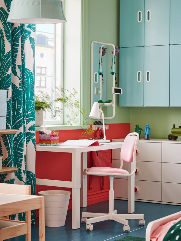Una habitación para niños con amplio almacenaje y un espacio de estudio formado por un escritorio PÅHL blanco y una silla de escritorio infantil ÖRFJÄLL rosa.