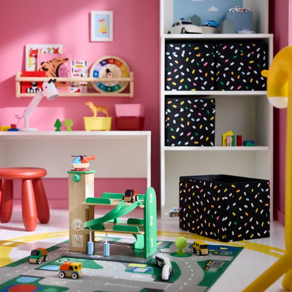 A LILLABO garage with car and helicopter placed on a play mat in a children’s room with colourful shelves and storage units.