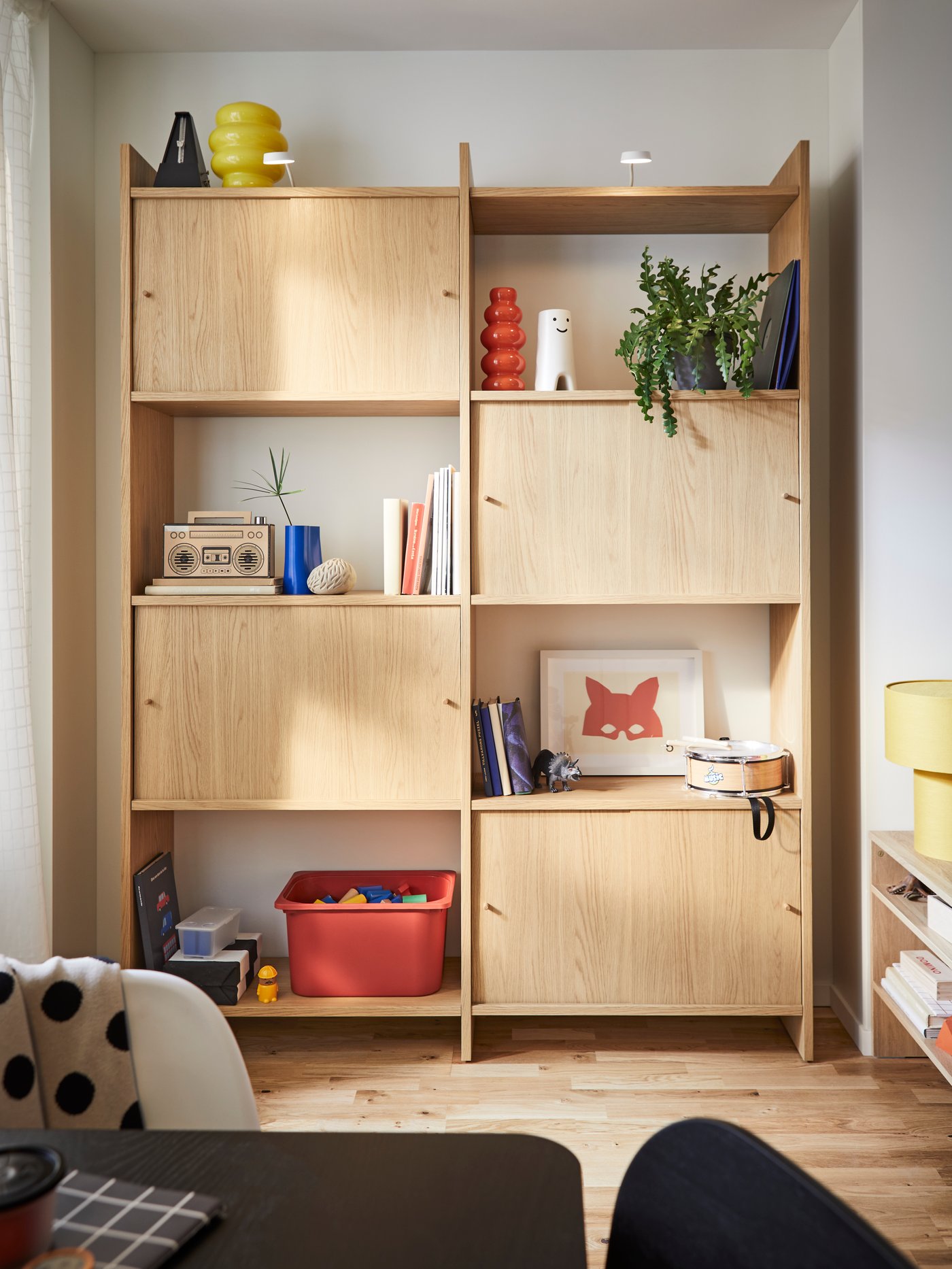 A LÅDMAKARE storage combination, holding many things including a yellow KÄLLARHALS vase, stands against a wall.