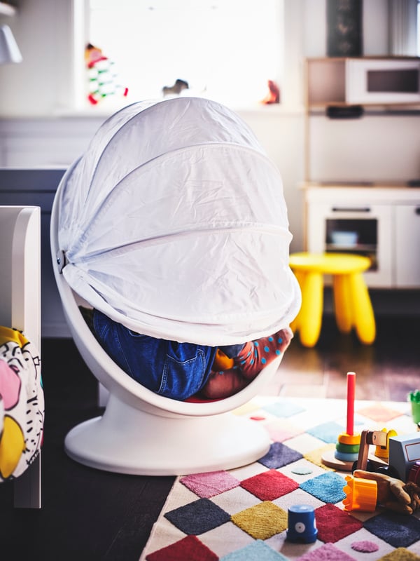 A kids'room with a child sitting in a mostly closed IKEA PS LÖMSK swivel armchair half set on a coloured BUSENKEL rug.
