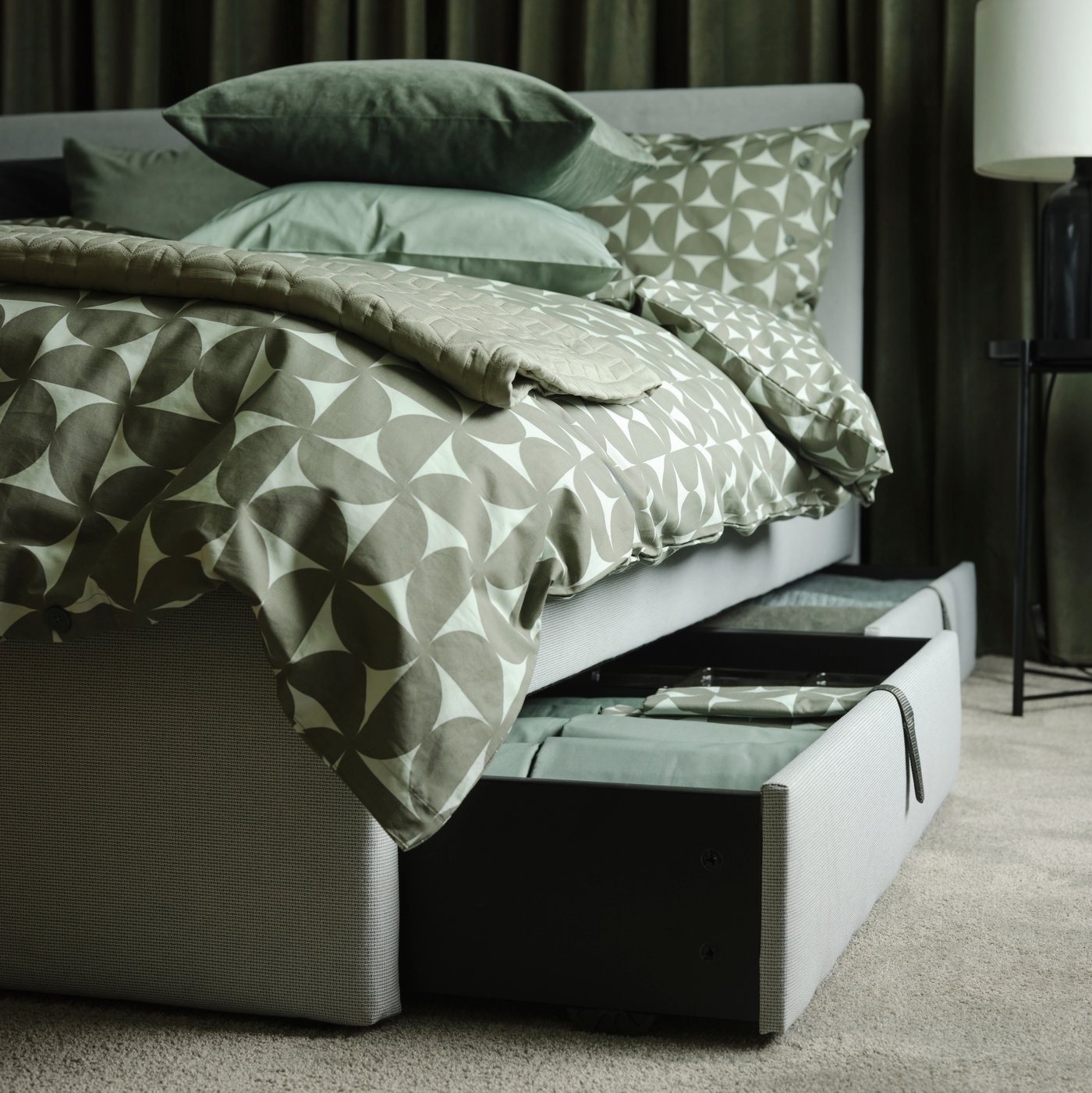 Grey queensized GLADSTAD storage bedframe with pull-out storage drawers, covered with green patterened ANGSNEJLIKA duvet covers and SANELA cushions on the bed.