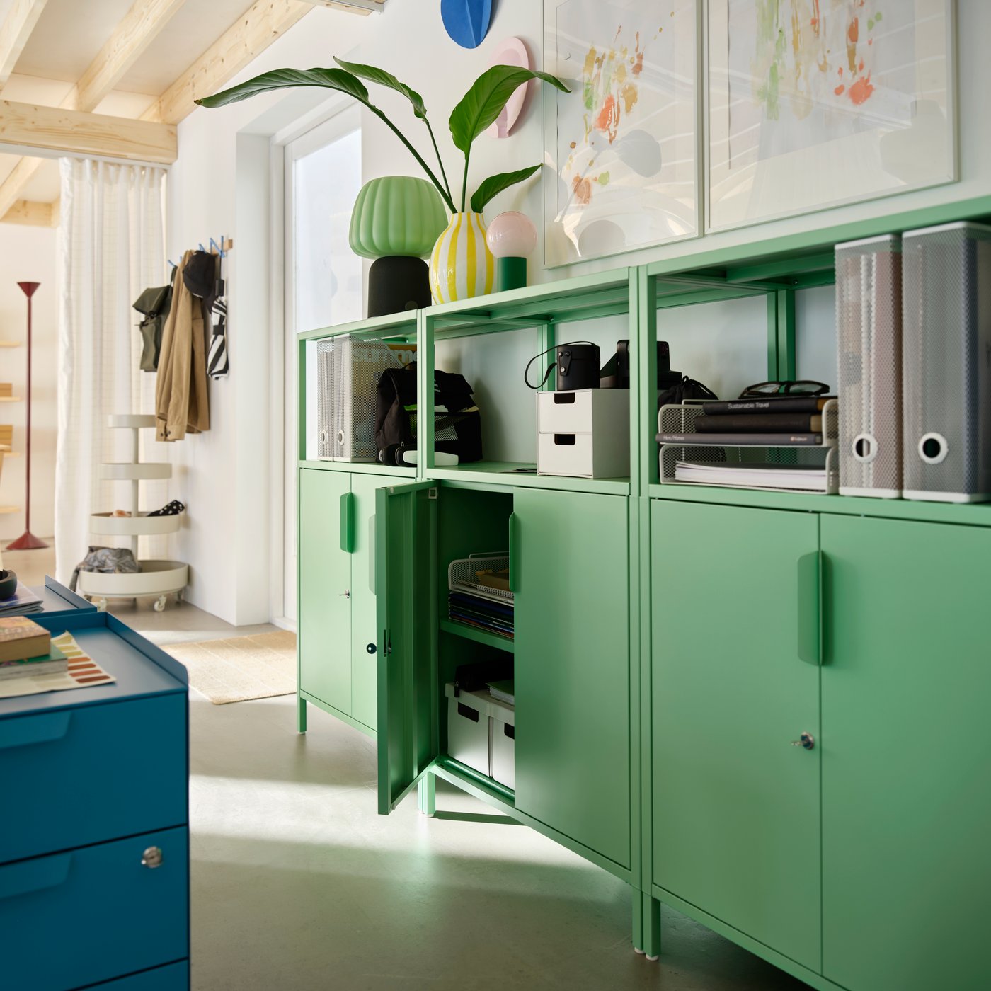 Row of green TROTTEN office cabinets with open shelving above. One cabinet door is open, revealing stationery stored inside.