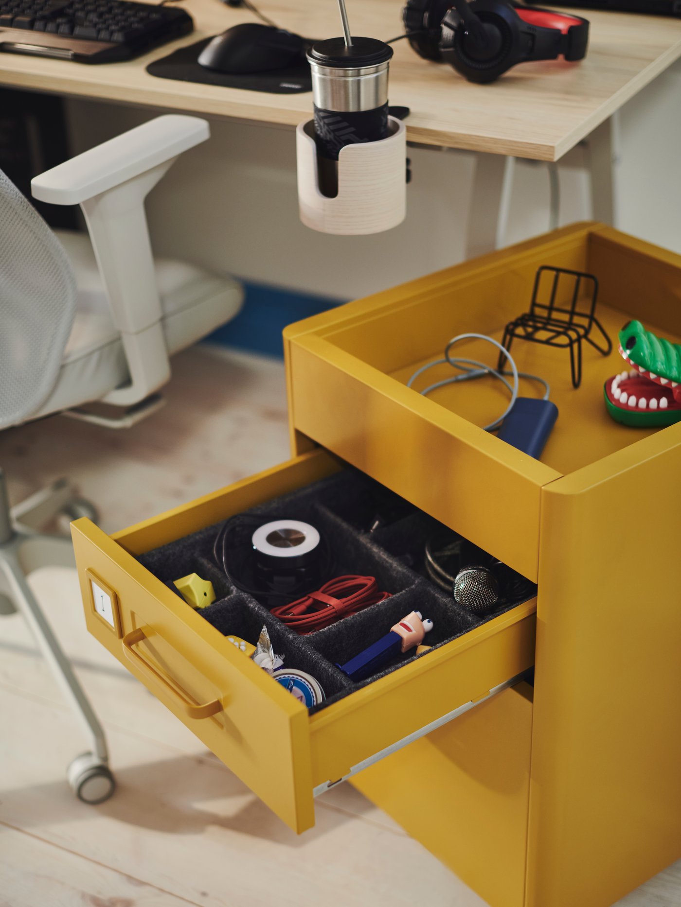 Caisson à tiroirs sur roulettes IDÅSEN brun doré dont un tiroir ouvert révèle des câbles et des accessoires de gaming.