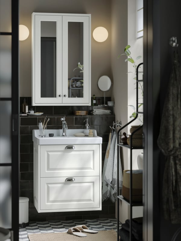 A small traditional-style bathroom with white TÄNNFORSEN storage furniture, round lamps on the wall and black details.