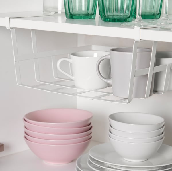 A PÅLYCKE clip-on basket attached to a white shelf, the basket holds various mugs with other tableware items on the shelves.
