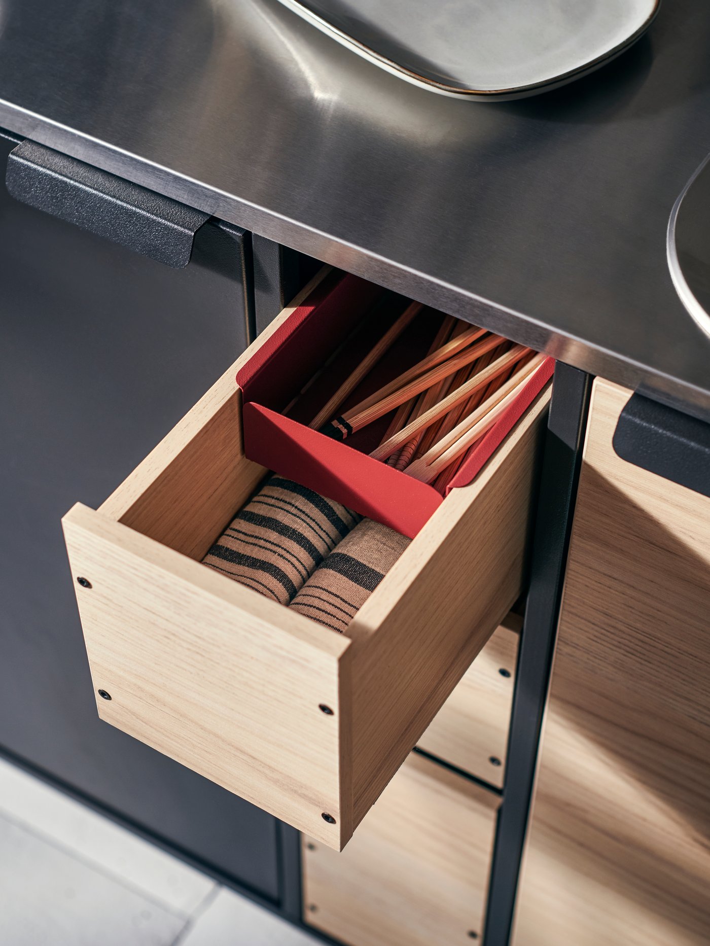 An ÄSPINGE kitchenette with drawer open and MARIATHERES tea towels in stripe/grey beige and a GLADELIG plate in grey on top.