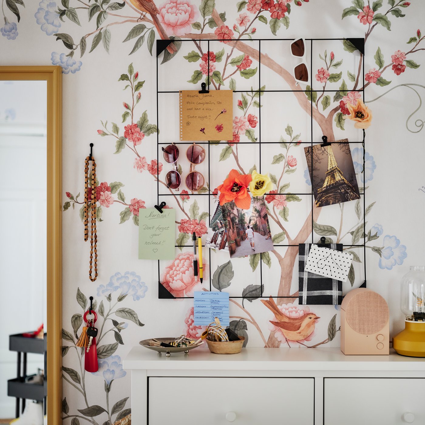 Fixé sur un mur au motif fleuri, tableau-mémo SÖSDALA noir avec des cartes et des lunettes de soleil, surmontant une armoire à chaussures GULLABERG blanche.