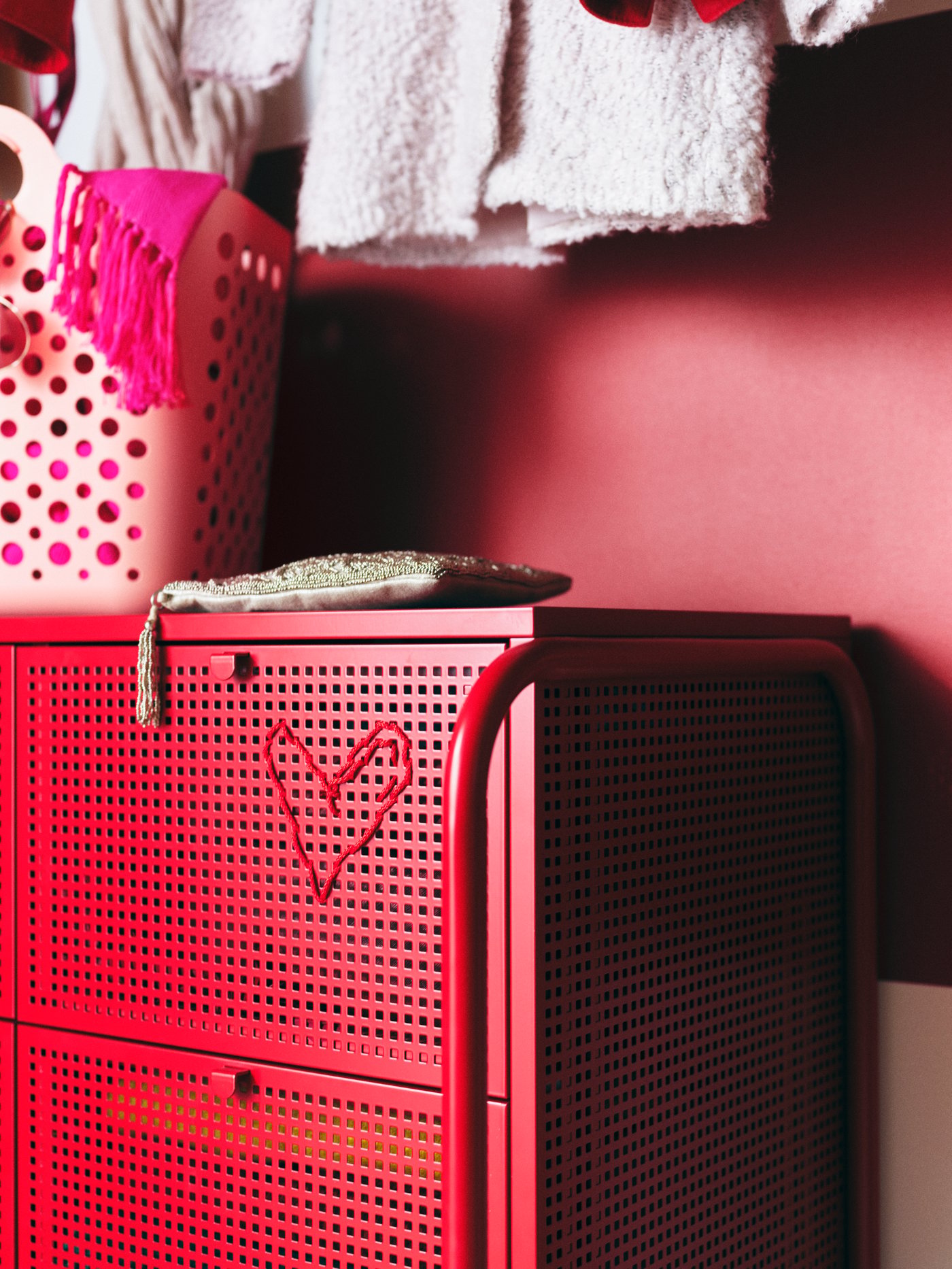 Una cómoda NIKKEBY roja con un corazón rojo bordado y una canasta flexible para ropa SLIBB rosa encima.