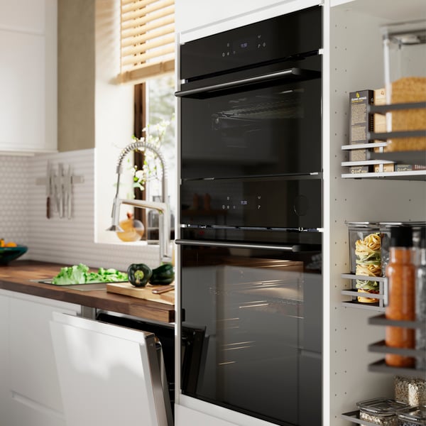 A SPJUTBO true fan oven and a true fan oven with microwave function are placed in a kitchen with matt white VOXTORP fronts.