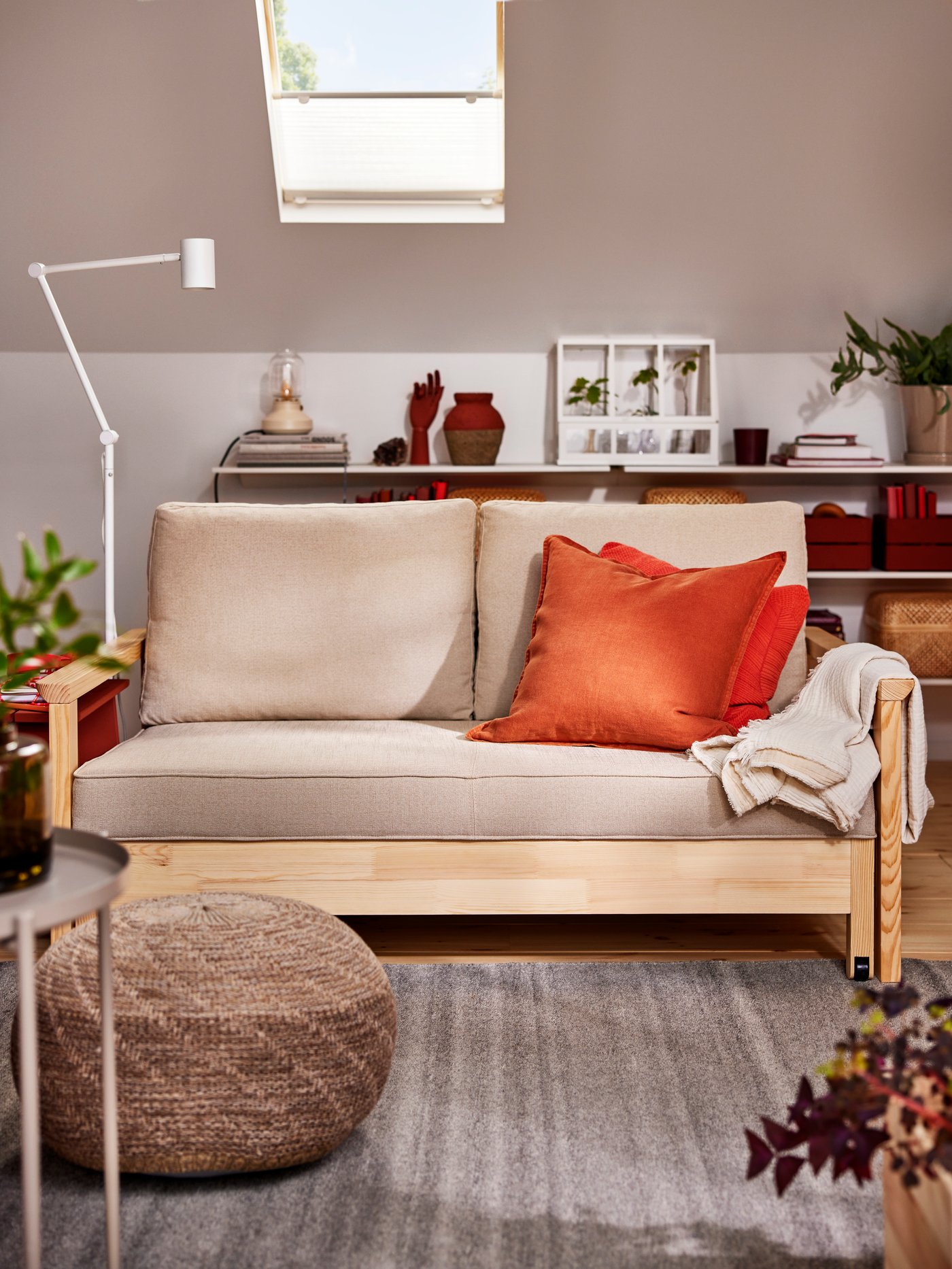 A TORNSBORG sofa-bed with extra cushions on it stands opposite a beige SANDARED pouffe on a grey TIDTABELL rug.