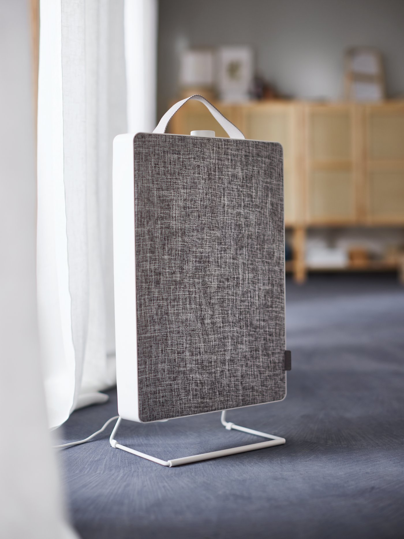 A person’s hands put away two pairs of shoes on a shoe storage shelf by a white FÖRNUFTIG air purifier attached to the wall.