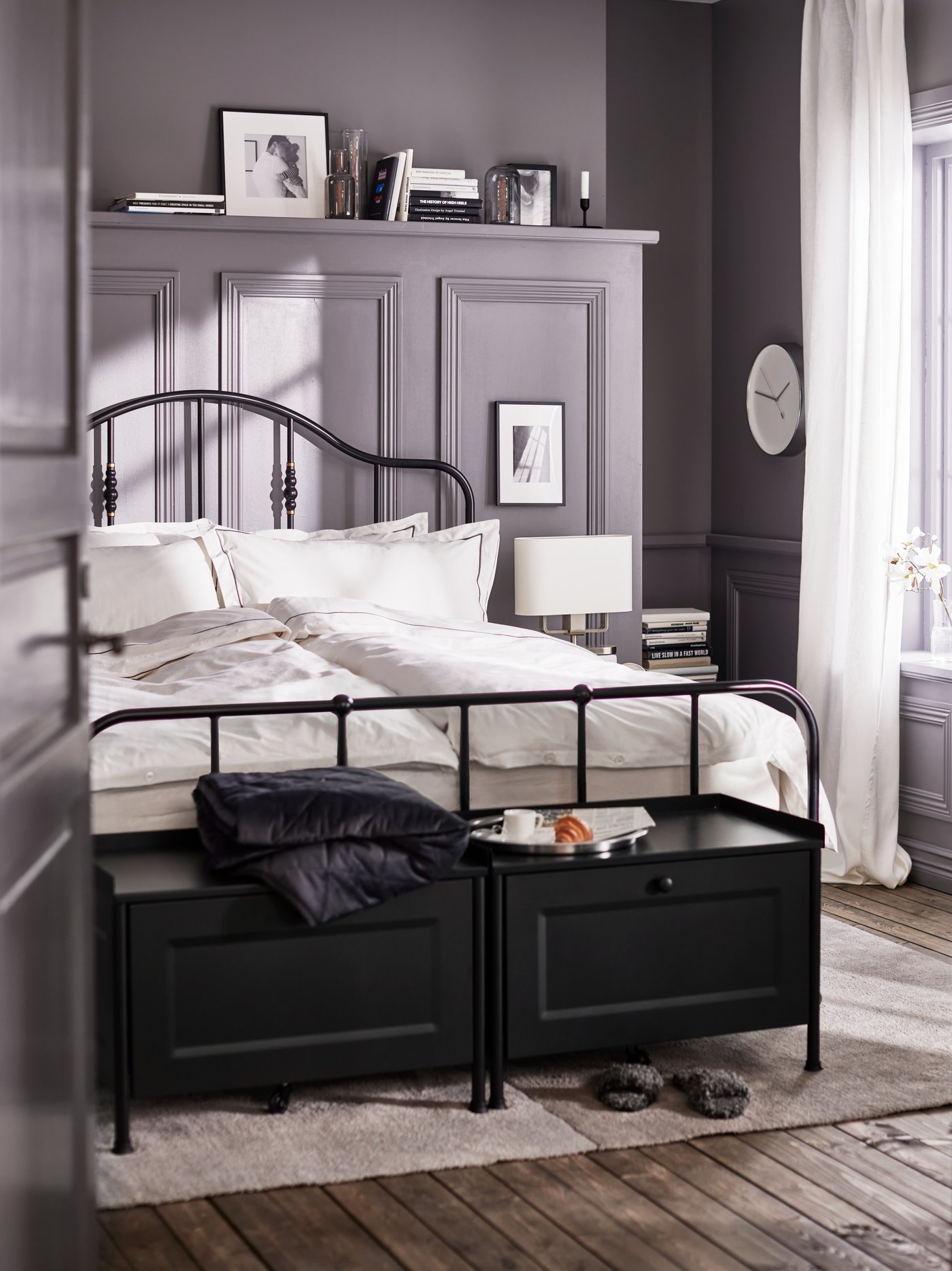 Two black KORNSJÖ storage benches and a bed with a black bed frame made with white/dark gray bed linen on a light gray rug.