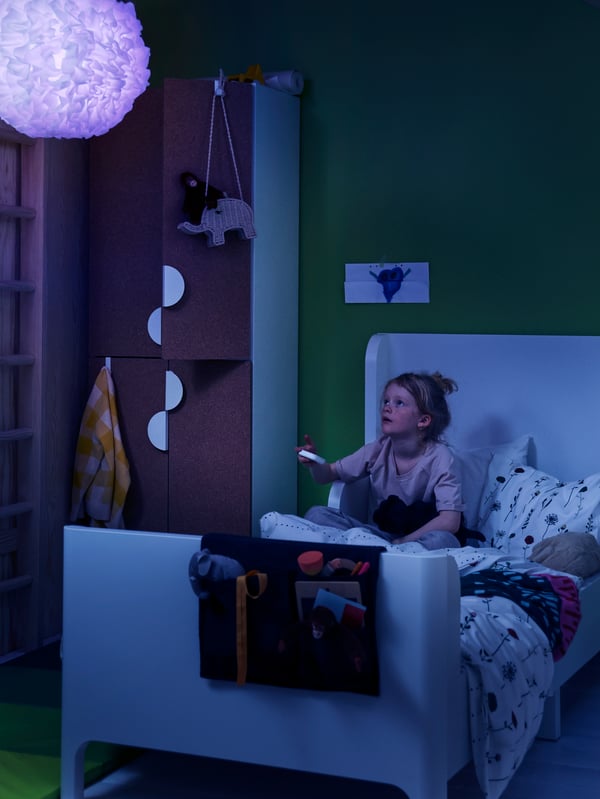 A girl uses a STYRBAR remote control to change the colour of a TRÅDFRI LED bulb to blue in a VINDKAST pendant lamp.