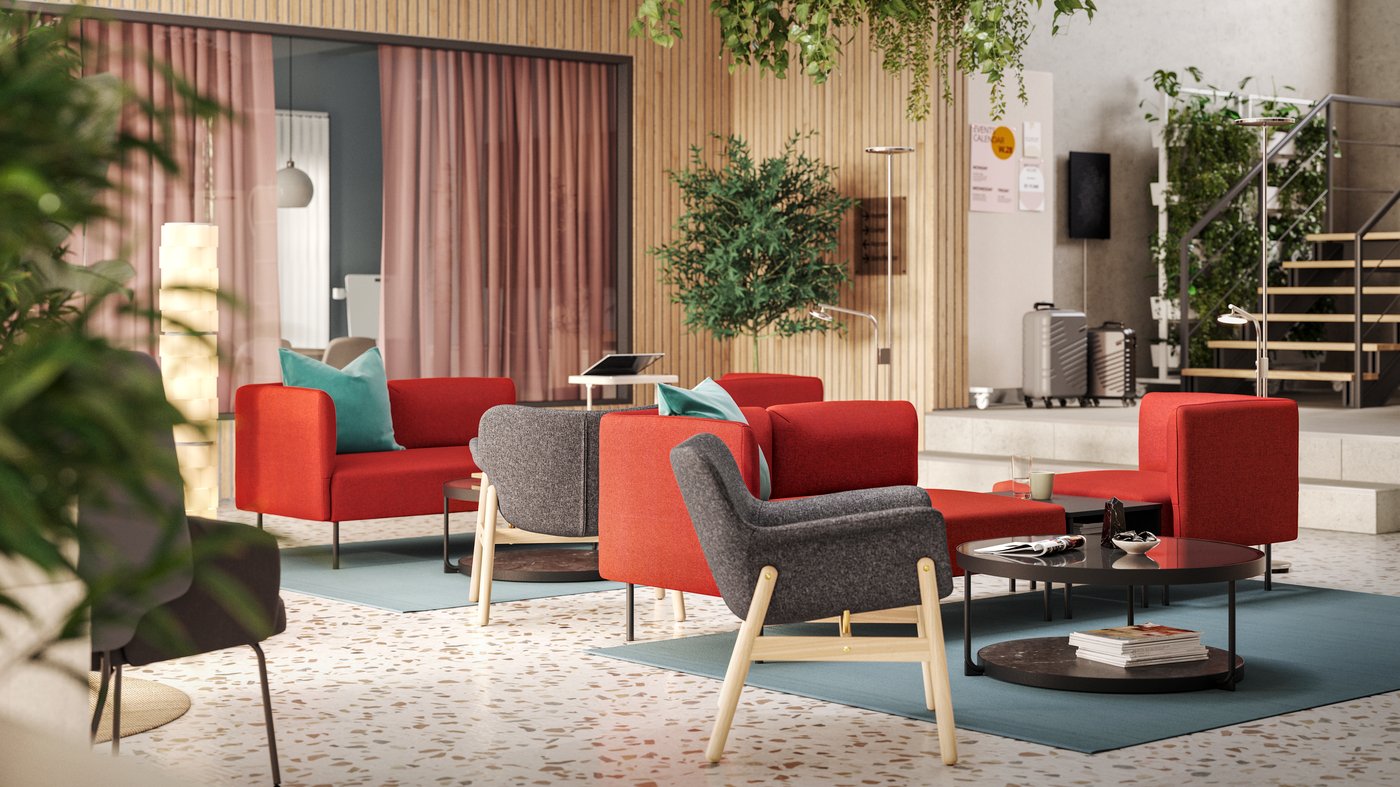 Seating groups with dark grey VEDBO armchairs and red modular sofas are in the middle of a light-filled, modern hotel lounge.