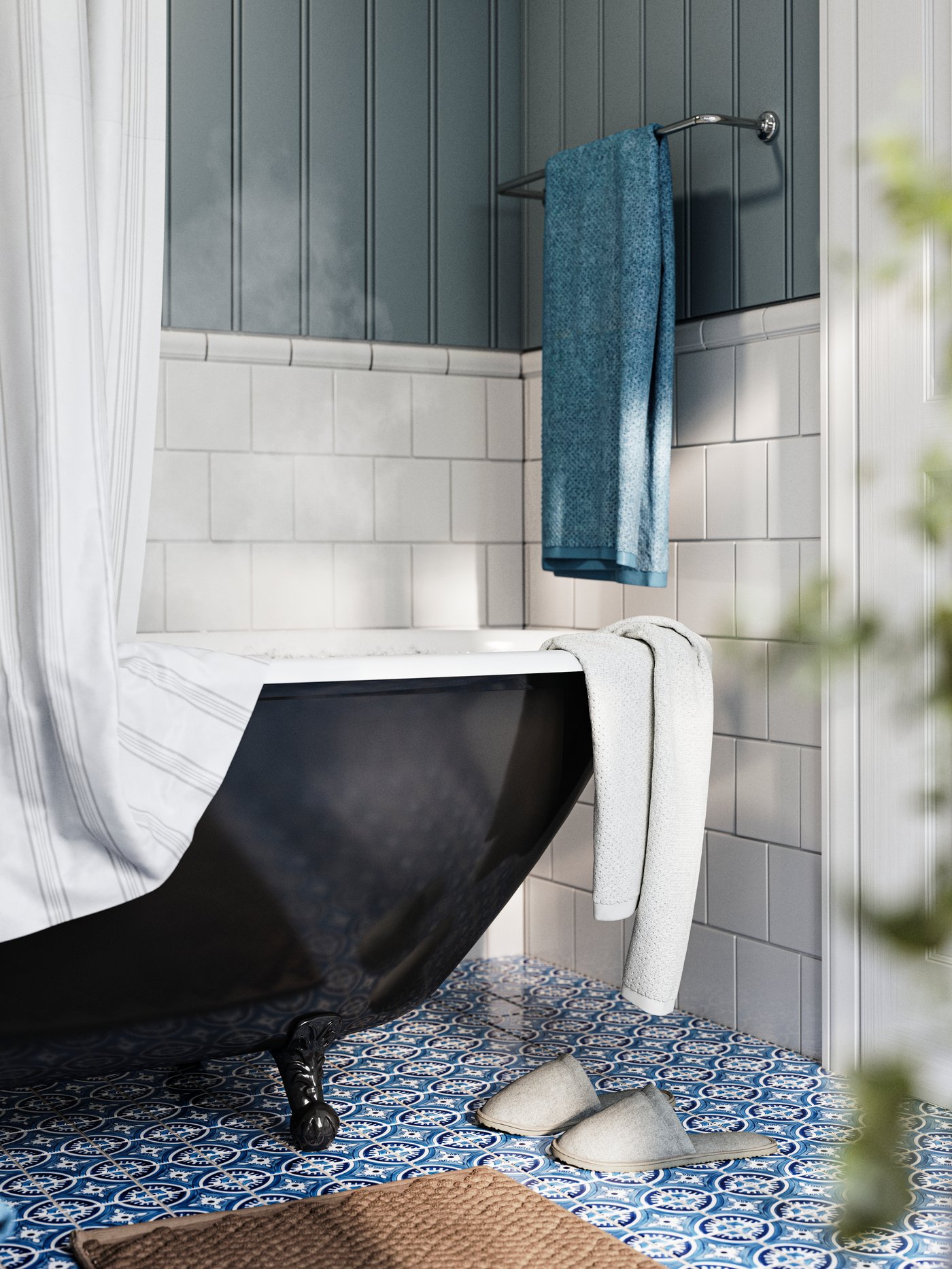 A bathroom with white and blue walls and a blue patterned floor has a bathtub and a blue GULVIAL bath towel on a rail.