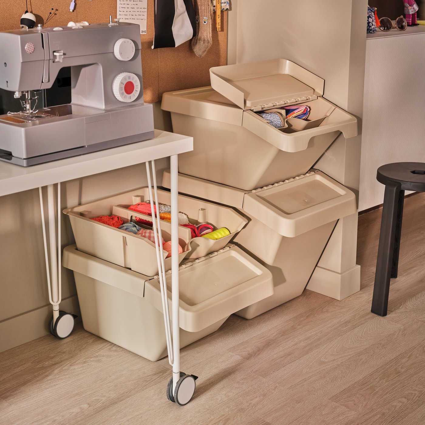 A room with a sewing machine on a table and beige SORTERA sorting bins with lids arranged nearby, filled with supplies.