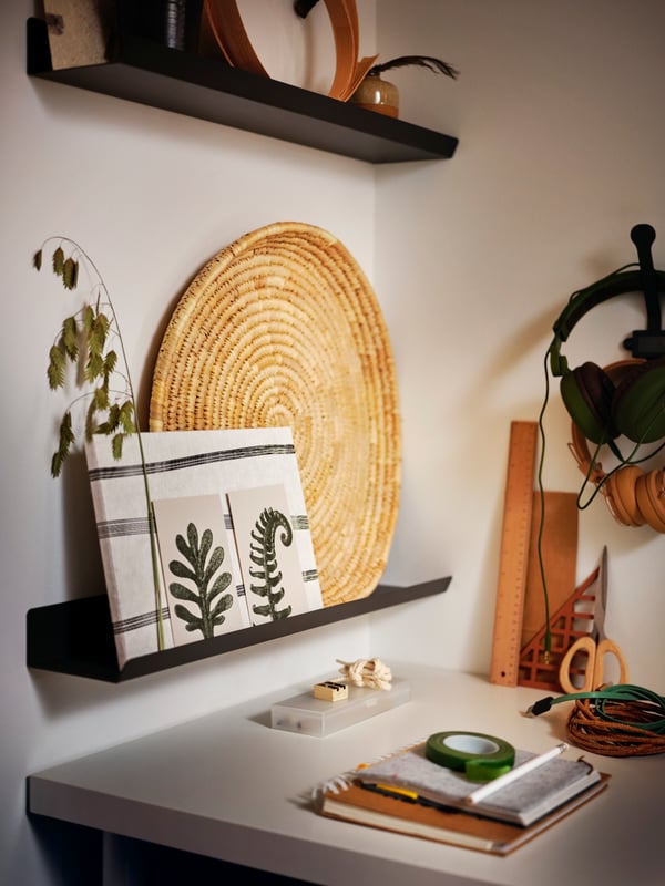 Un bureau dans un coin, avec des objets décoratifs sur des étagères MALMBÄCK gris foncé fixées au mur au-dessus.