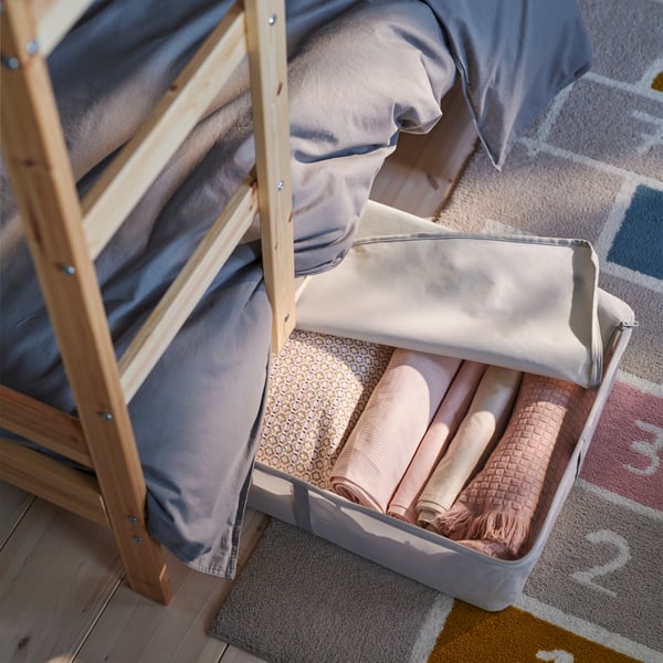 The bottom of a pine MYDAL bunk bed showing a white SKUBB storage case half under the bed holding folded pink textiles.
