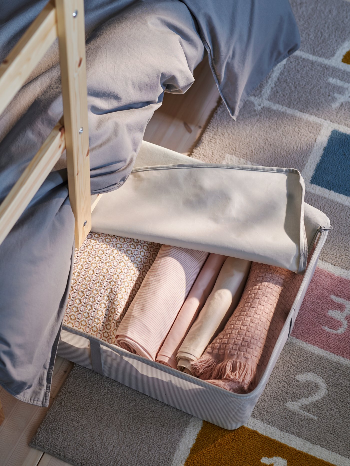 The bottom of a pine MYDAL bunk bed showing a white SKUBB storage case half under the bed holding folded pink textiles.