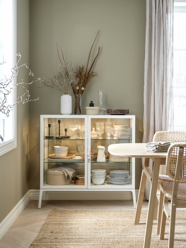 Dans le coin d’une salle à manger, une vitrine blanche avec éclairage intégré remplie de vaisselle.