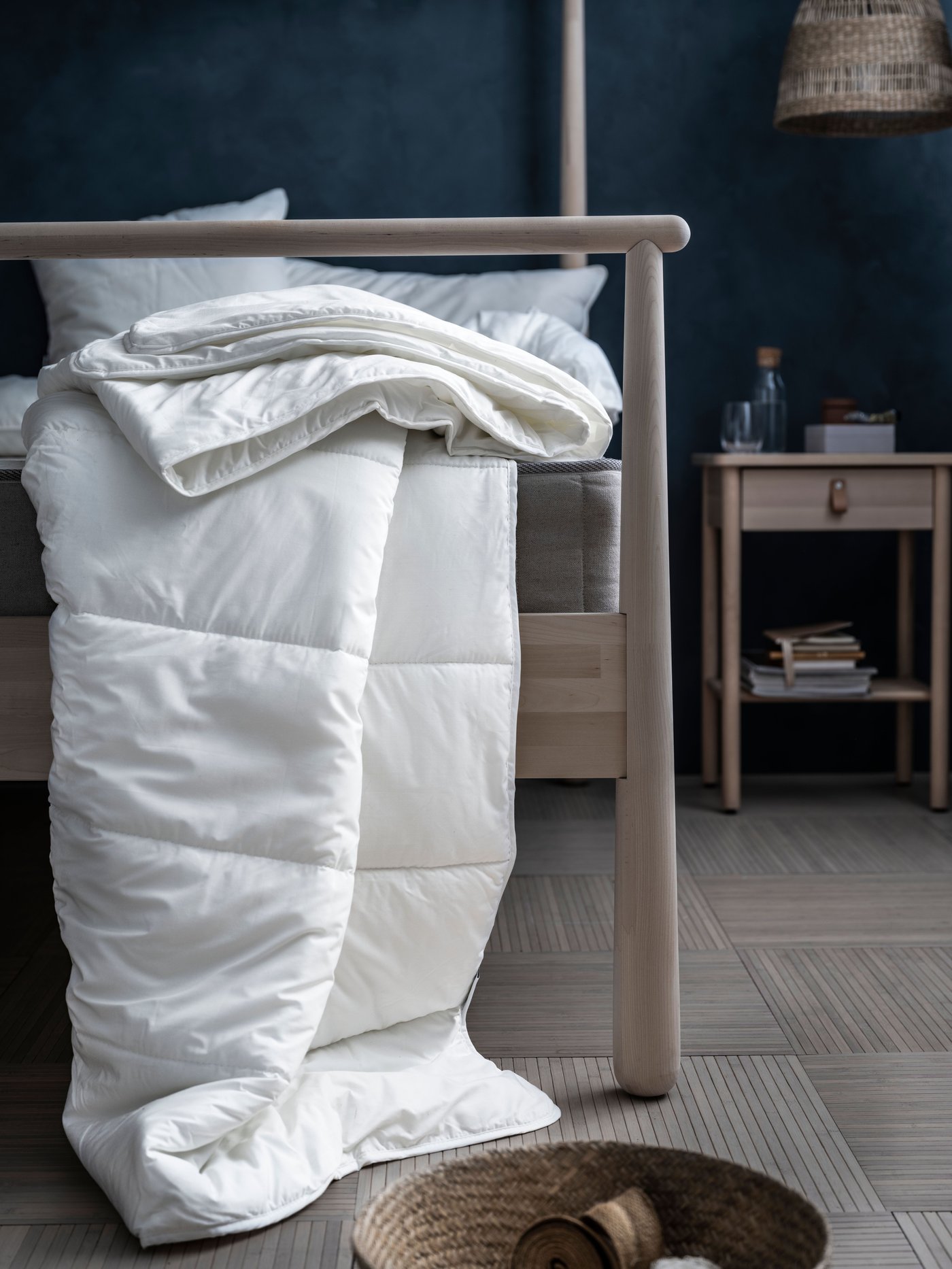 Couette blanche drapée sur le pied du lit GJÖRA et tombant jusqu’au plancher. Une table de chevet BJÖRKSNÄS est à côté du lit.
