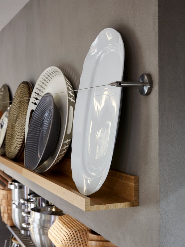 MÅLERÅS picture ledges in bamboo with plates and trays on it, supported by a curtain wire, above a shelf with cookware.