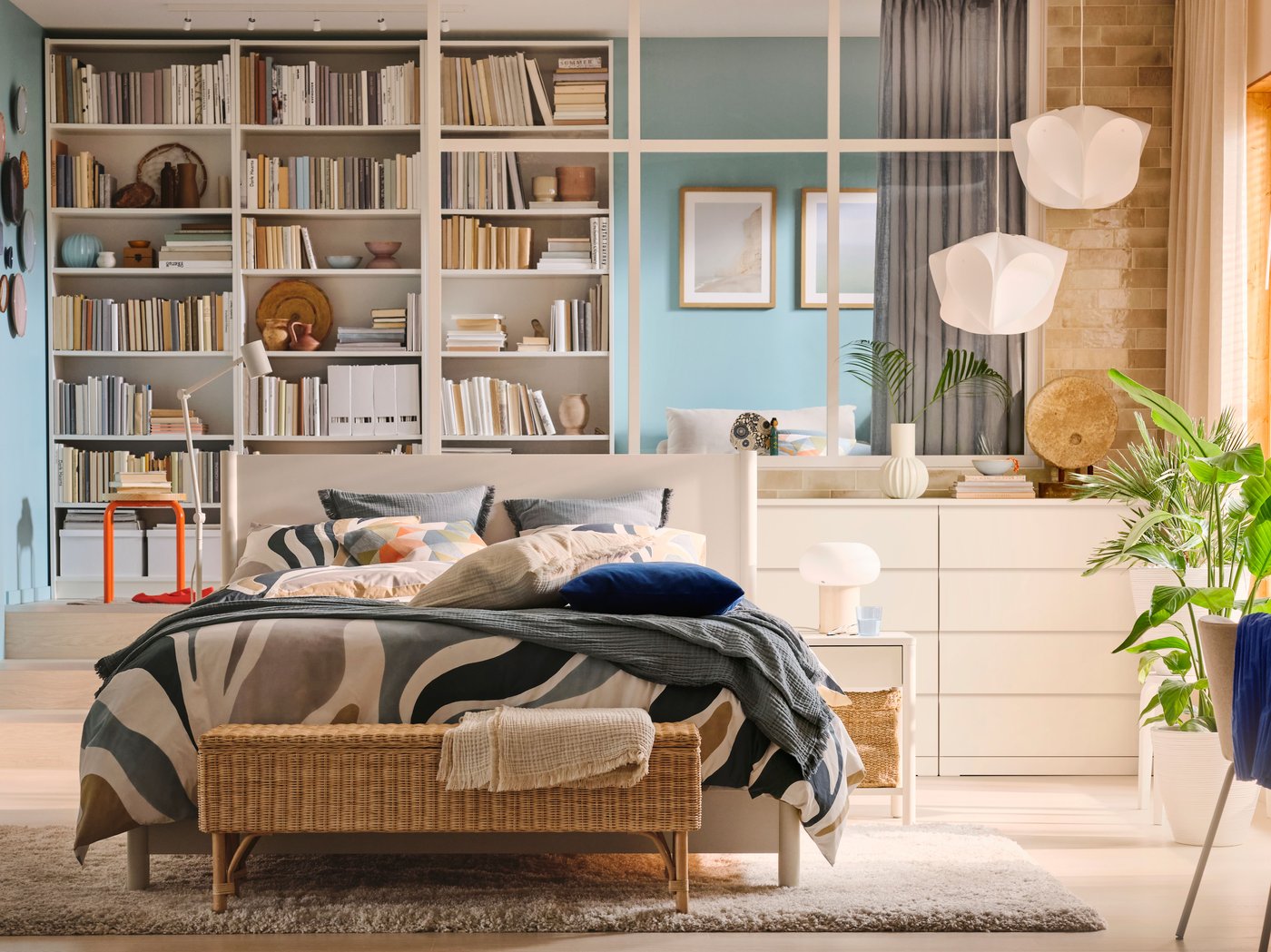 An off- white TONSTAD bed covered in MYGGLASVINGE bed linen in an airy bedroom in front of three white BILLY bookshelves.