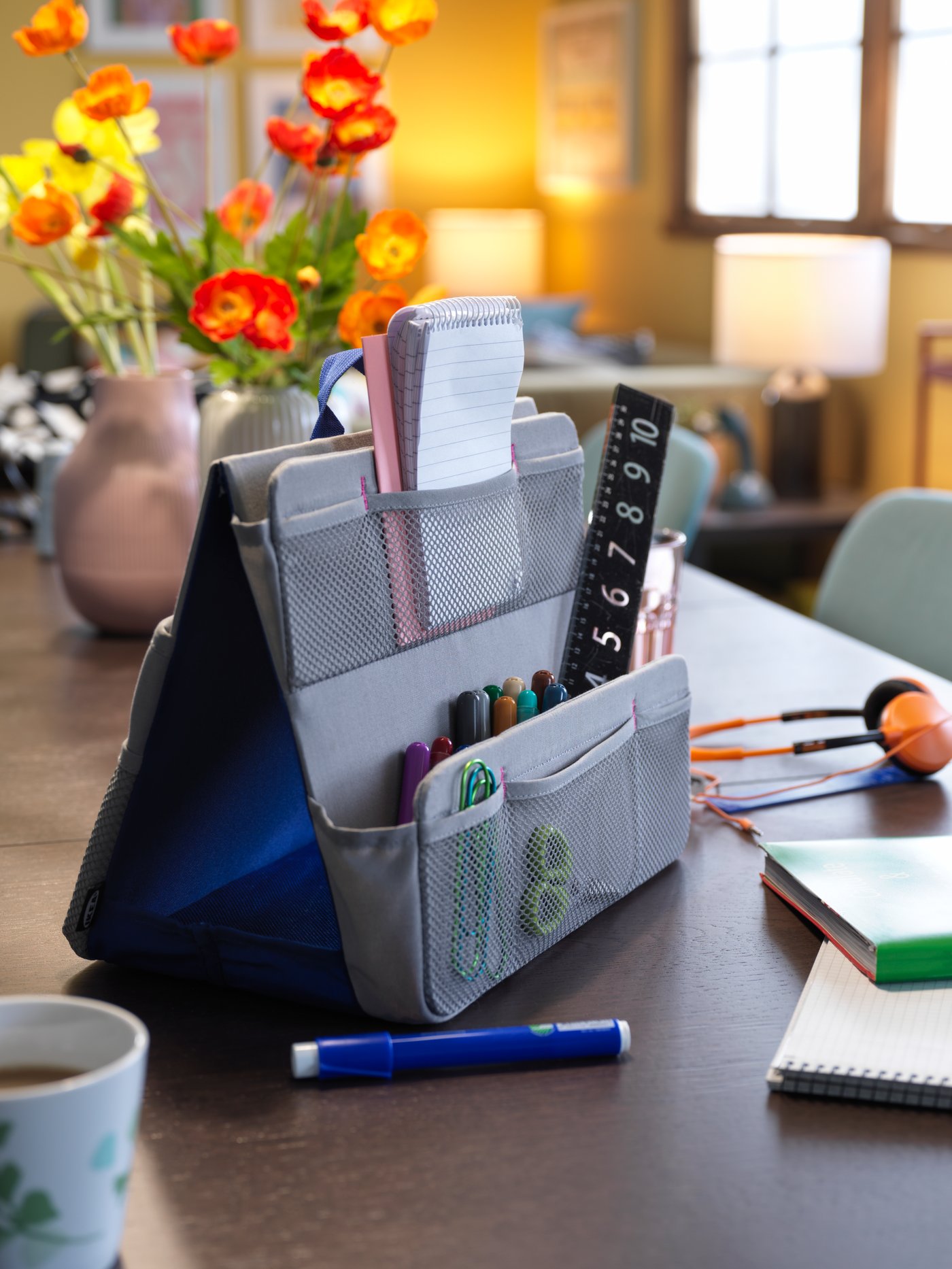 An IKEA ÖVNING desk organiser in grey with various pens and papers on a black brown dining table.