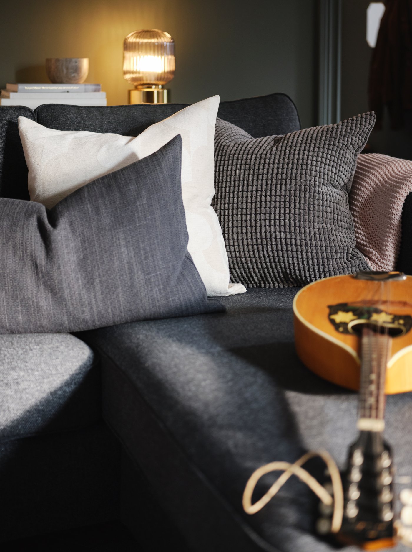 A cluster of textiles, including anthracite HILLARED and grey GULLKLOCKA cushions, on the chaise-longue end of a PÄRUP sofa.