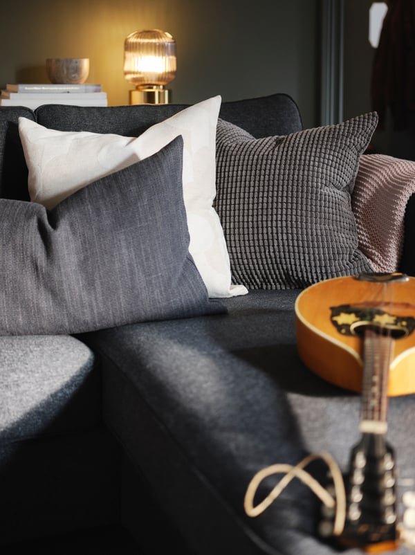 A cluster of textiles, including anthracite HILLARED and grey GULLKLOCKA cushions, on the chaise-longue end of a PÄRUP sofa.