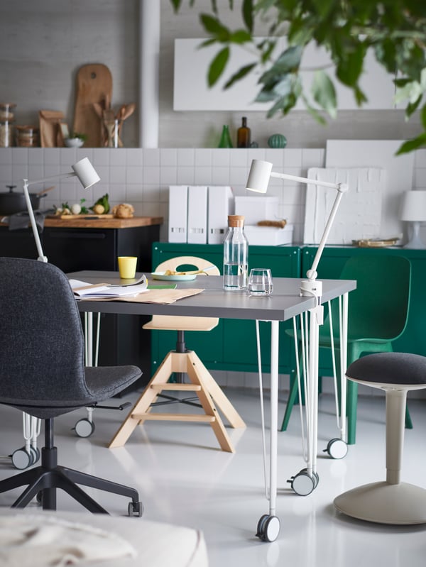 Two grey tables made from dark grey LAGKAPTEN table tops and white KRILLE legs with castors, work lamps and various chairs.
