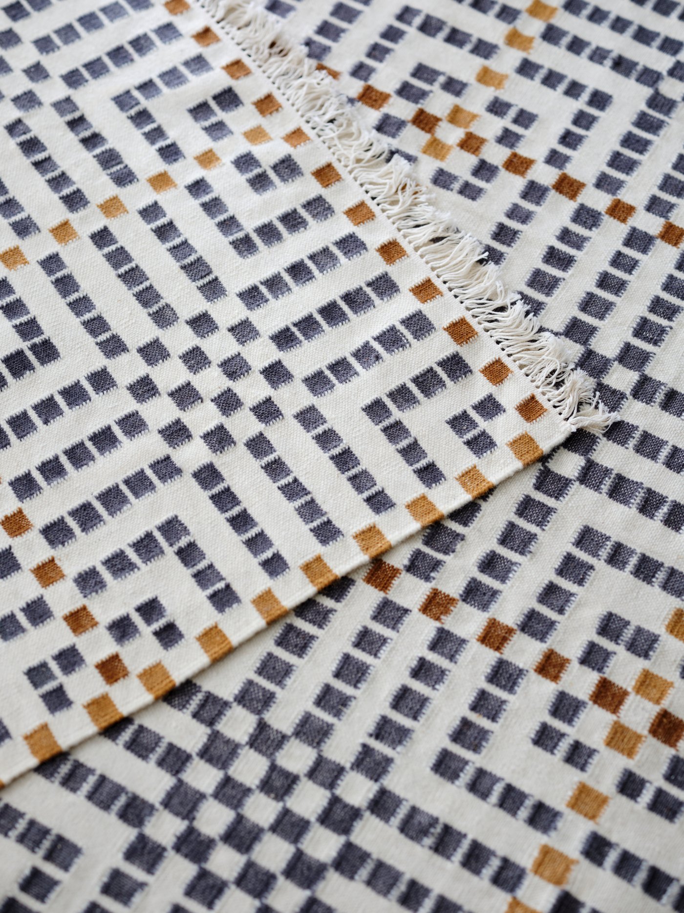A flatwoven VAMDRUP rug with a multicoloured traditional pattern is layered on top of another VAMDRUP rug.