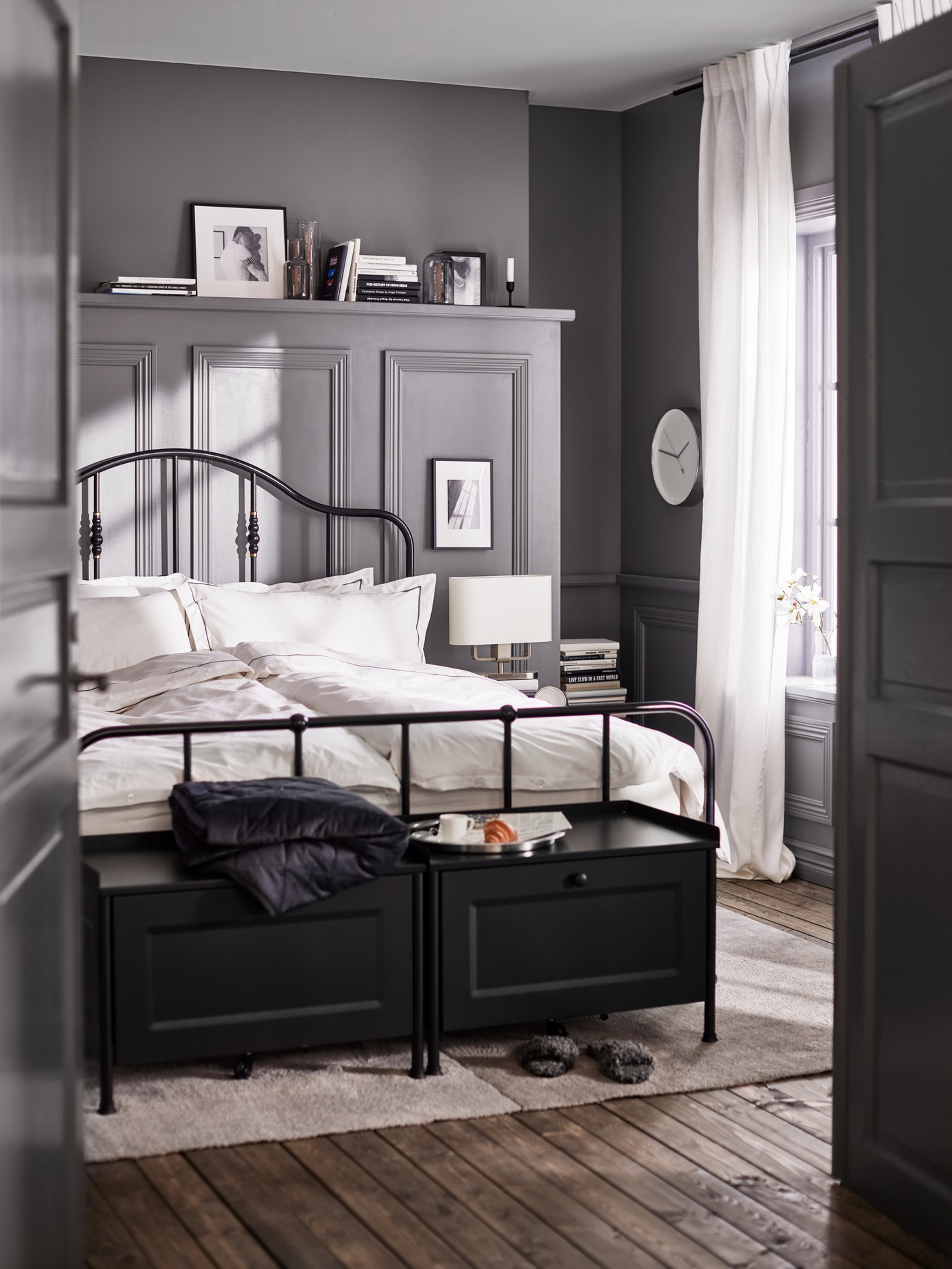 Two black KORNSJÖ storage benches and a bed with a black bed frame made with white/dark grey bed linen on a light grey rug.
