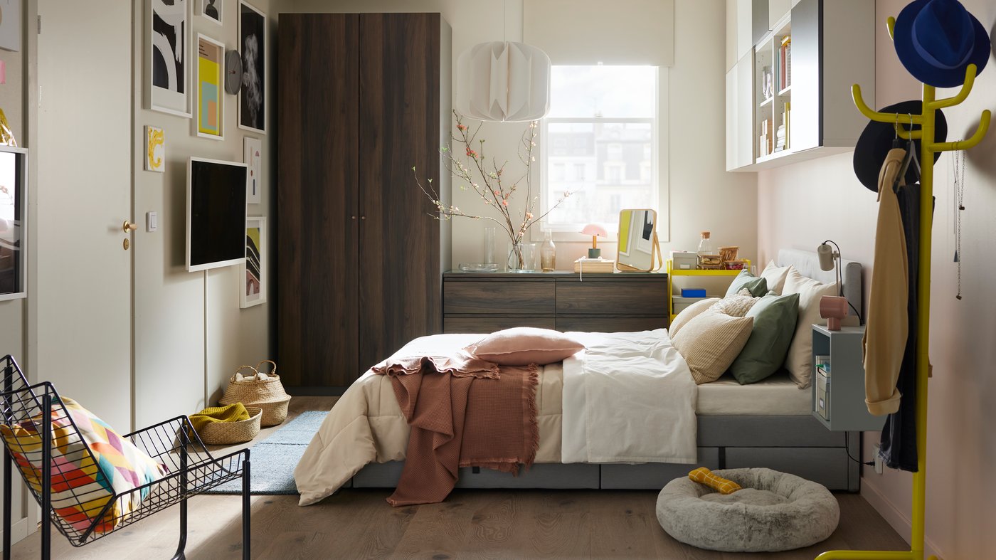 A grey GLADSTAD bed with green and cream textiles on it, in front of a PAX/STORKLINTA wardrobe and two dressers with 3 drawers.