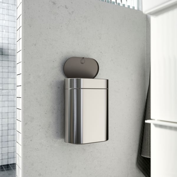 A softly lit white tiles bathroom and a BROGRUND touch top bin with an open lid hanging on a grey wall.