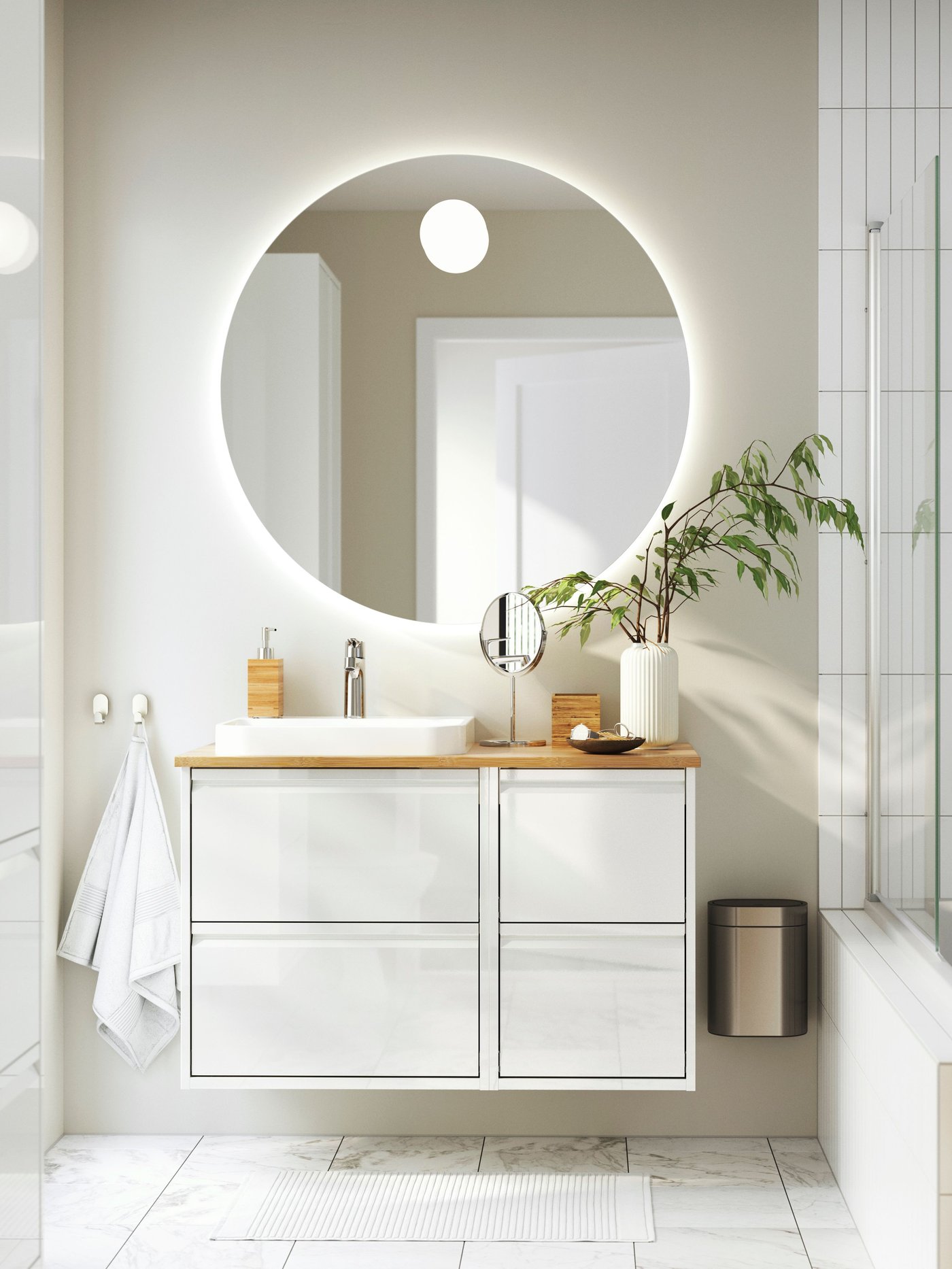 A contemporary bathroom with a large, back-lit mirror, white wash-stand with four drawers and floors with marble effect.