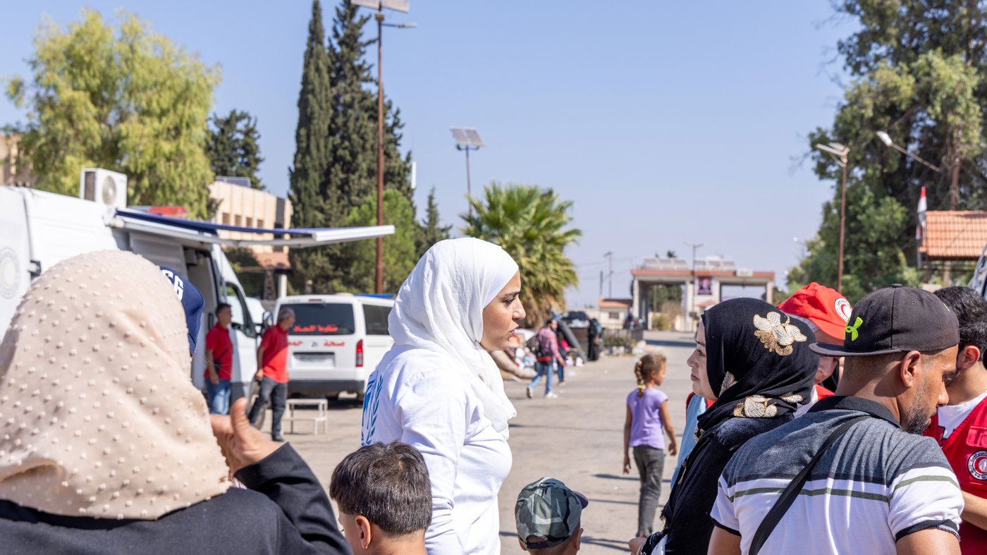 Lujain steht draussen auf einer Strasse und spricht mit einer anderen Person. Sie ist umgeben von Menschen.