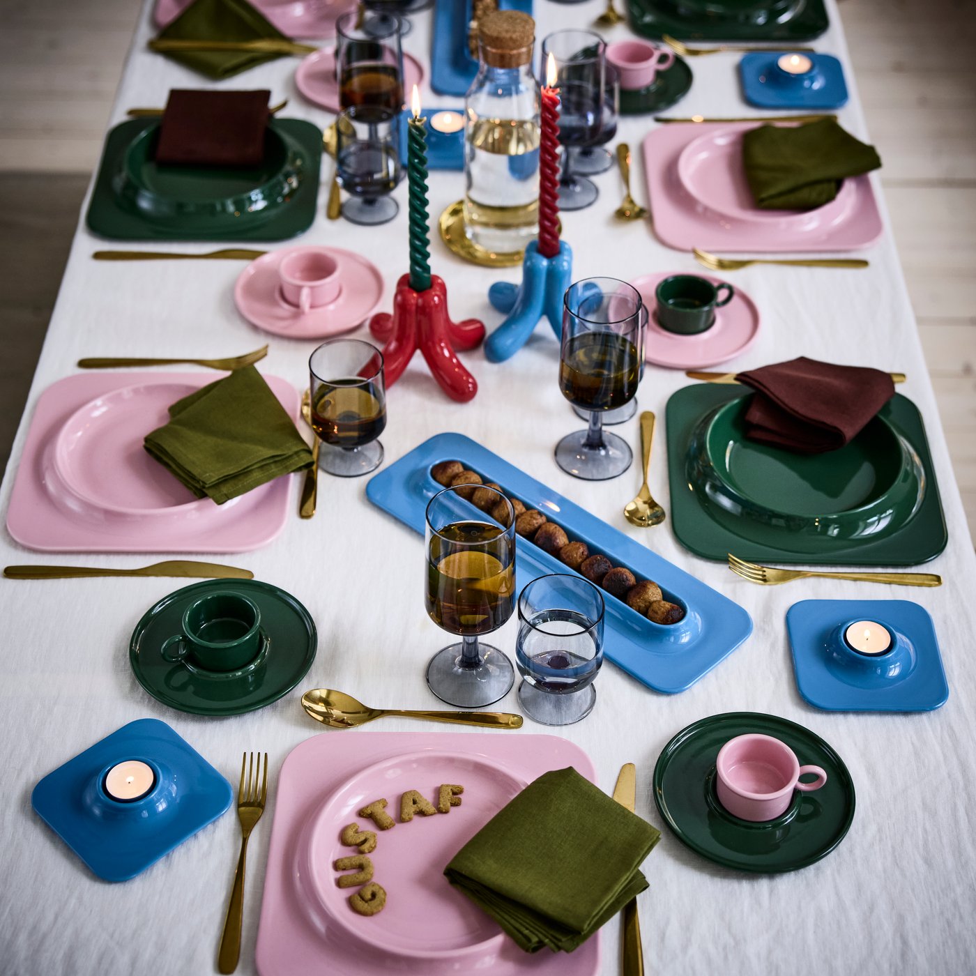 Een speelse kersttafel is gedekt met VINTERFINT-borden, kopjes met schoteltjes en kandelaars, ontworpen in samenwerking met Gustaf Westman.