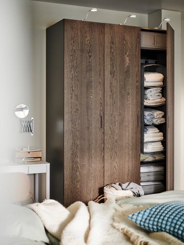 A PAX/TONSTAD wardrobe with an open door showing a a dark grey SKUBB hanging storage with 6 compartments inside.