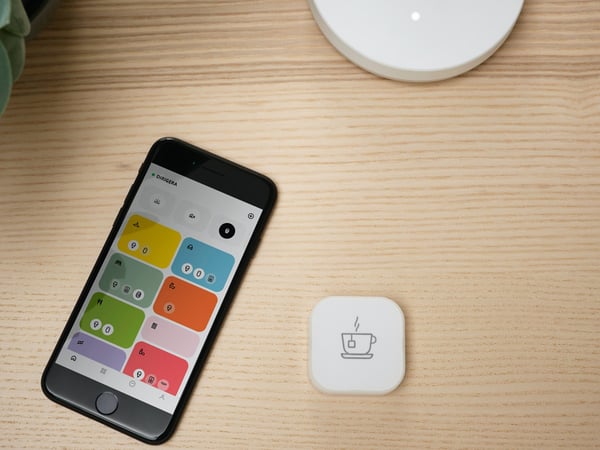Mobilni uređaj na kom se vidi aplikacija IKEA Home smart s TRÅDFRI dugmetom za prečicu i DIRIGERA bazom pored njega.