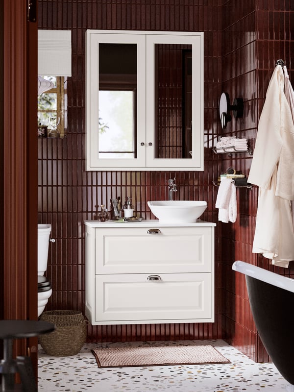 Dans une salle de bain carrelée de brun, meuble lavabo à tiroirs TÄNNFORSEN et vasque installés sous un meuble à miroir.