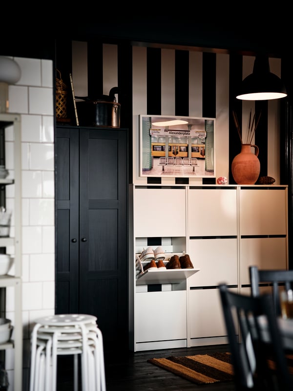 La partie d’une entrée à rayures noires et blanches avec des meubles à chaussures BISSA blancs et une armoire RAKKESTAD brun-noir.