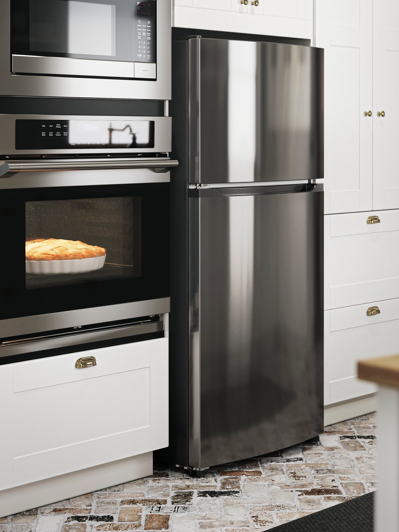 A FRYSBAR top-freezer refrigerator in stainless steel stands next to a built-in oven where a pie is being baked.